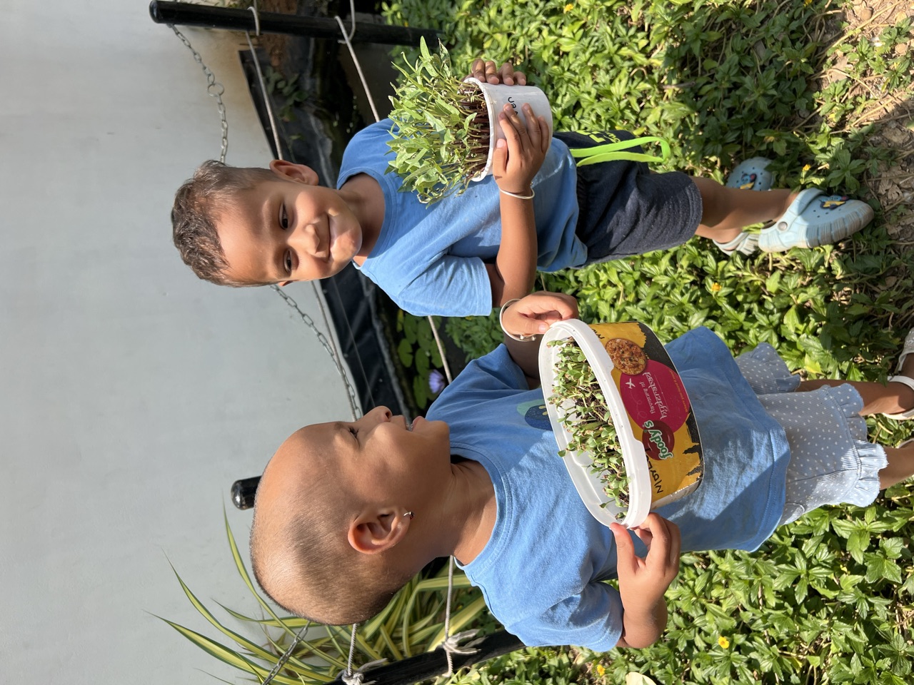 Two children proudly holding pots of microgreens they grew themselves