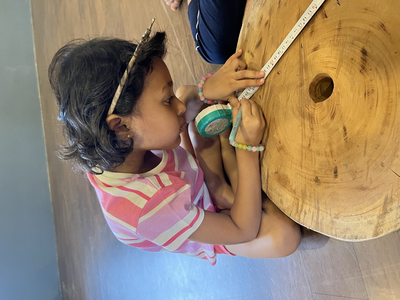 A child measuring a round slice of wood with a tape measure