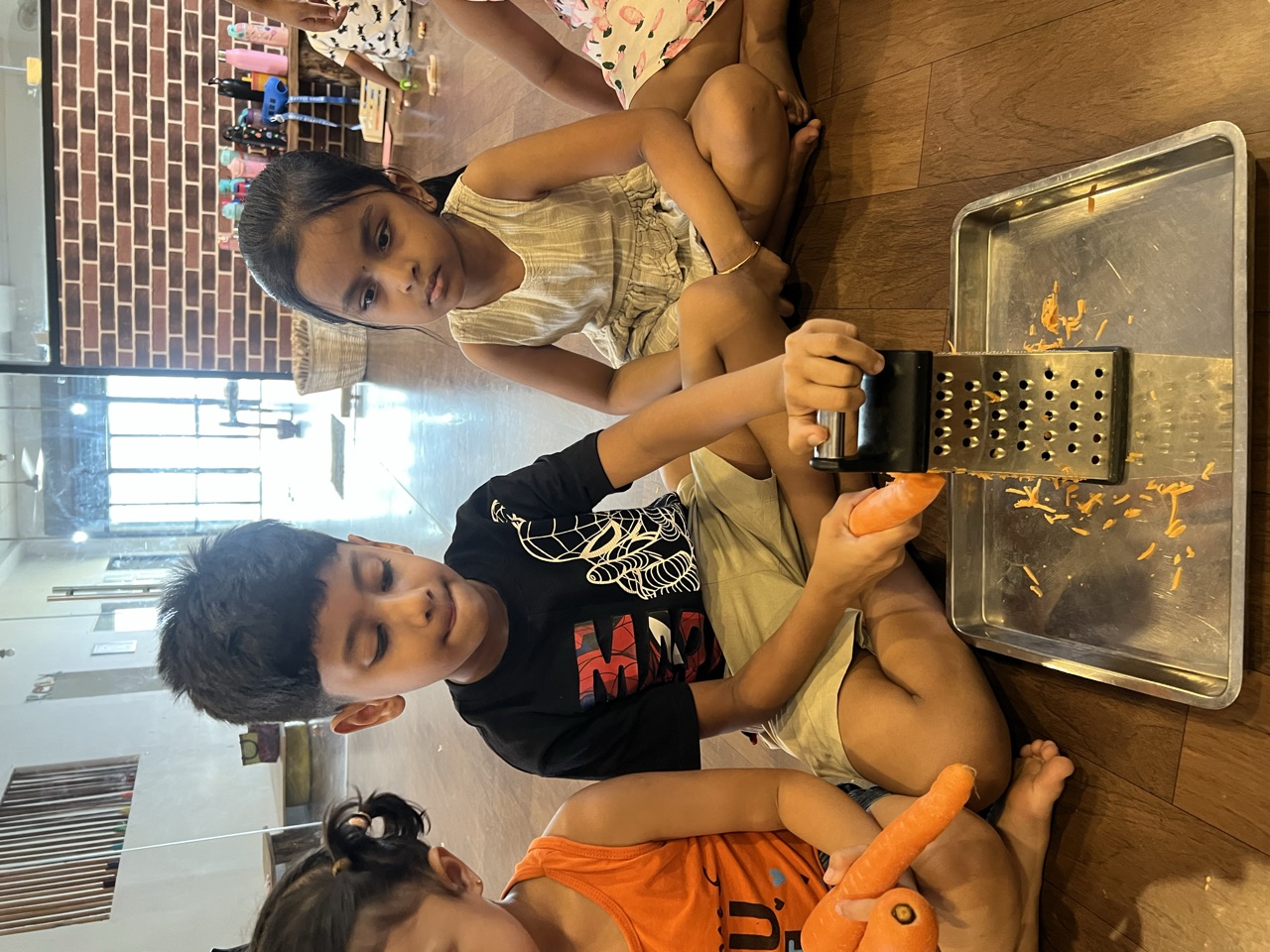 A child grating a carrot over a steel tray while friends look on