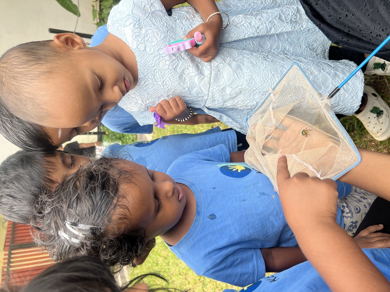 Children gathered close, examining a tiny beetle caught in a soft net