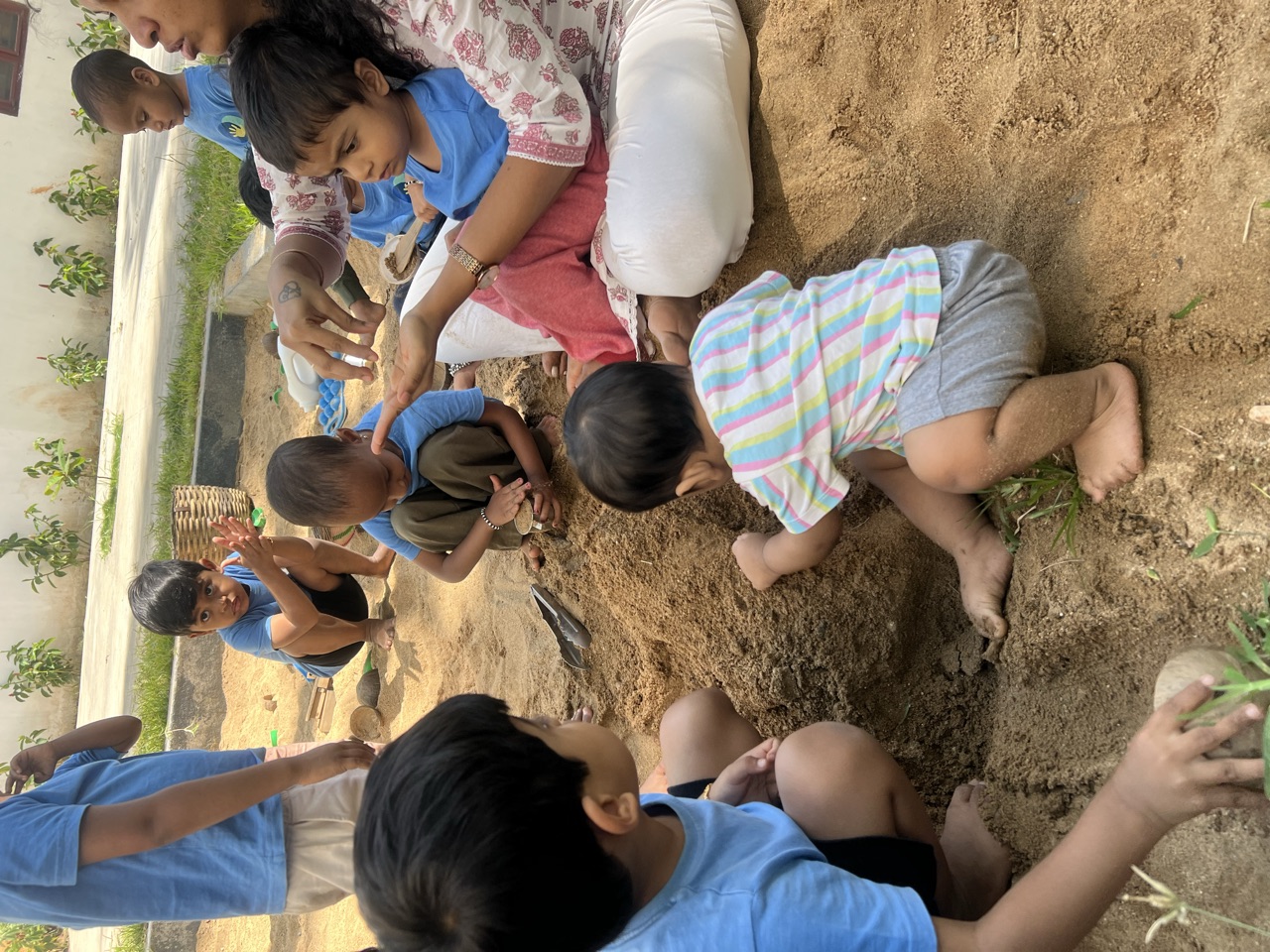 Children digging happily in the sand pit with teachers alongside