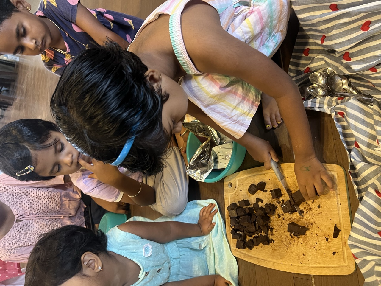 A child carefully chopping ingredients on a wooden board while friends watch