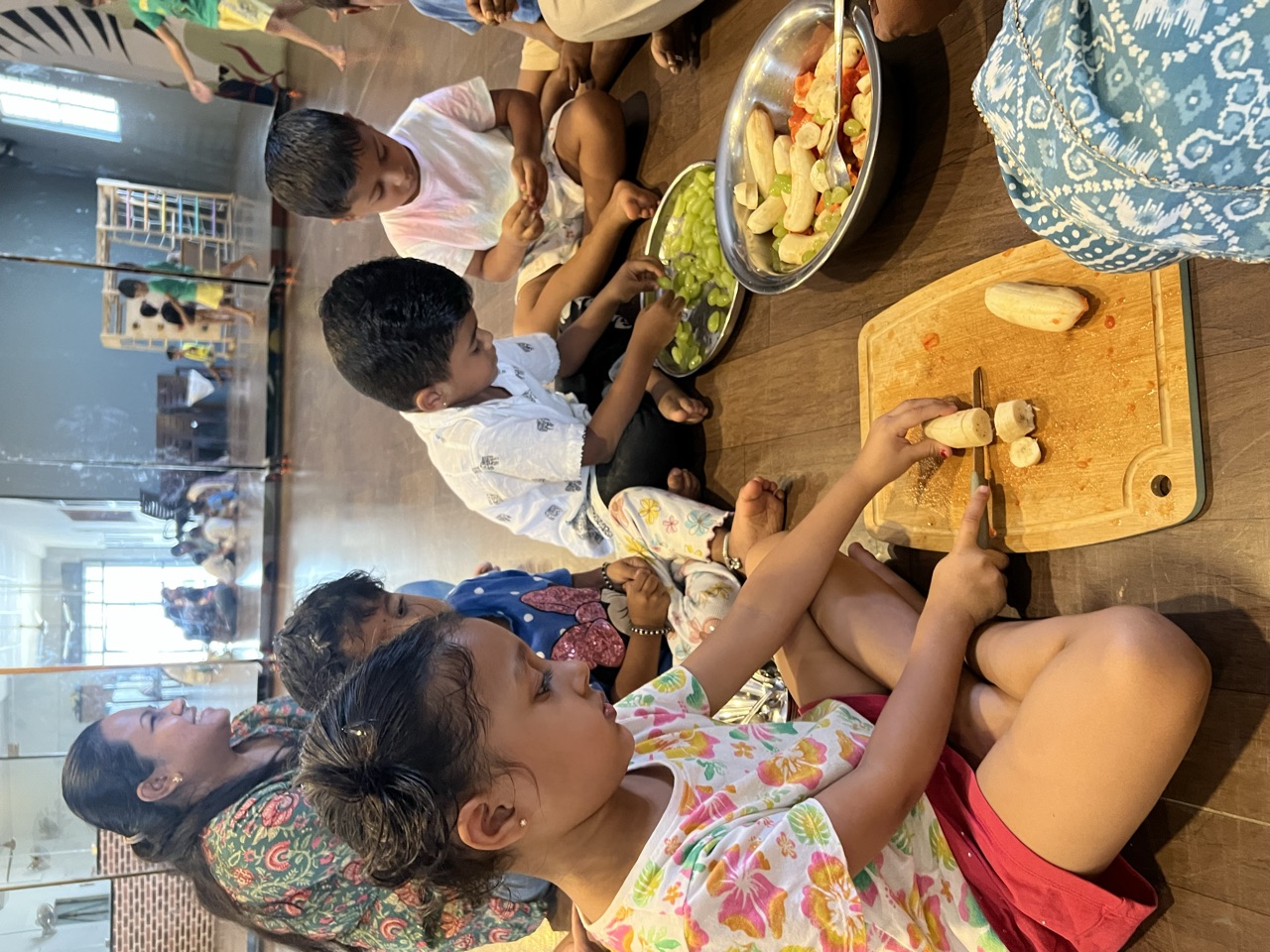 A child slicing bananas with bowls of fresh fruit ready beside her